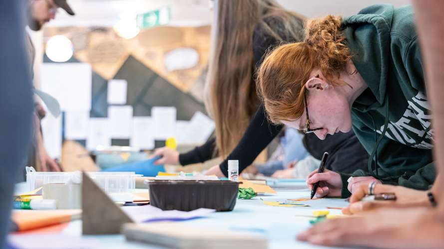 People engaged in a creative workshop, focusing on drawing and crafting at a table filled with art supplies.
