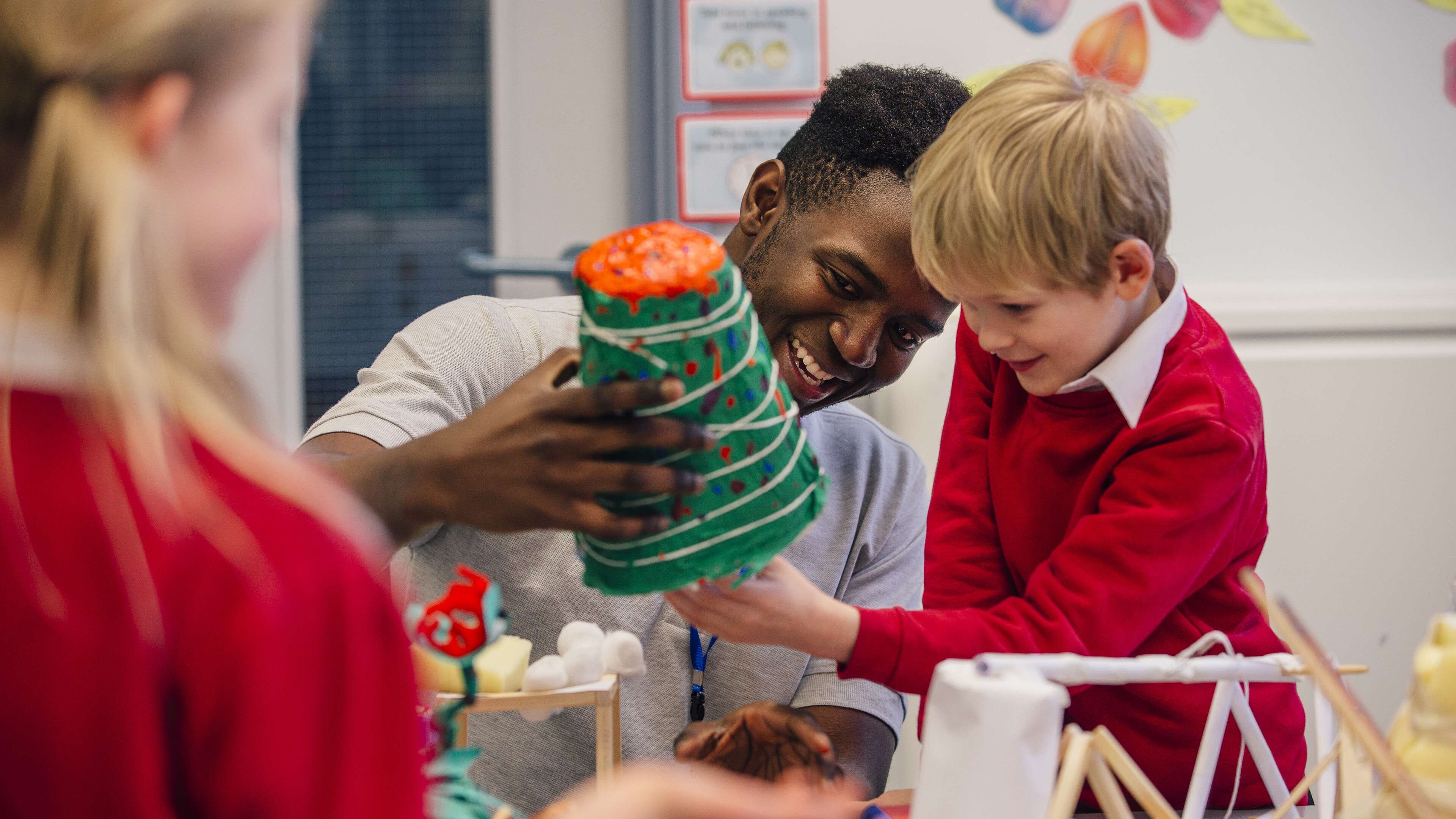 Young teacher is helping one of his primary school students during arts and crafts lesson.