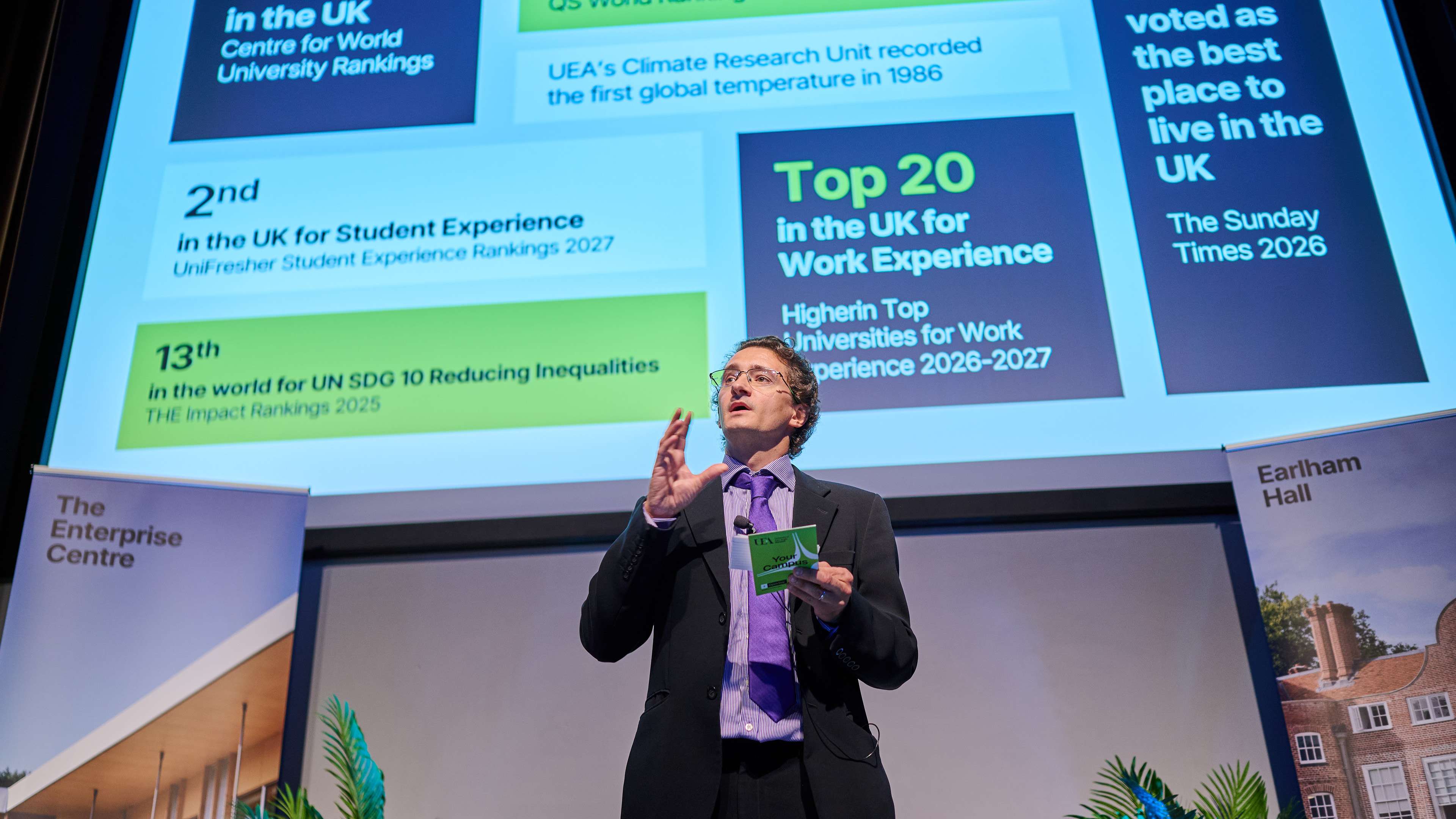 Someone gives a talk in front of a slide which highlights the benefits of attending a university.