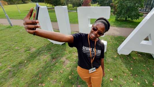 Student taking a selfie in front of UEA letters