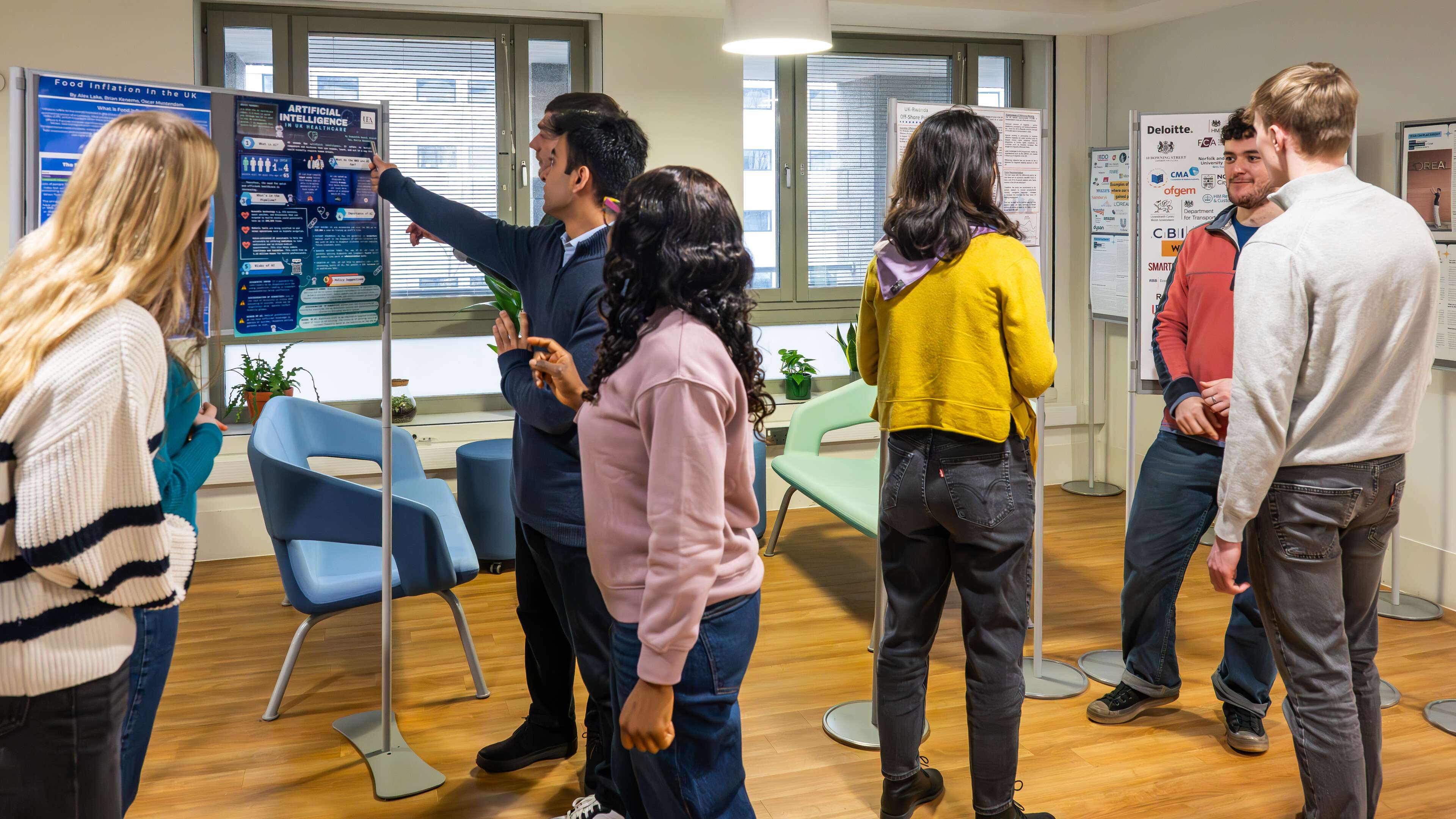 People discussing posters in an office setting, with chairs and plants in the background.