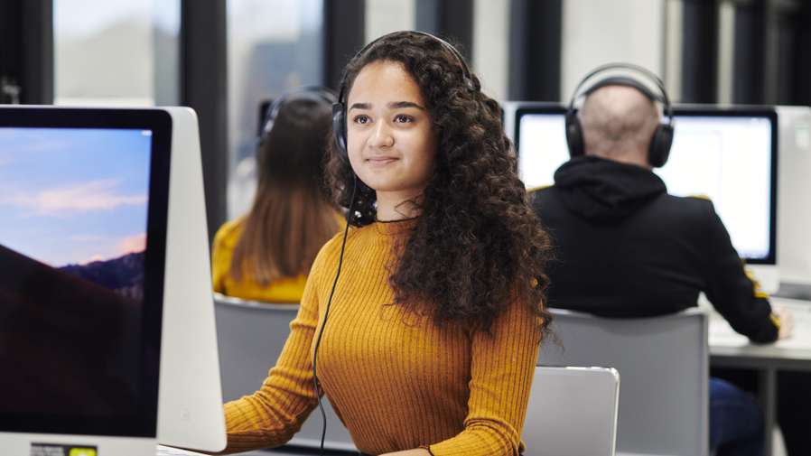 Mature student in media lab on computer with headphones.