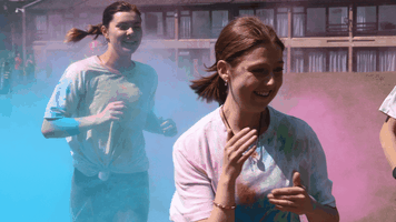 Two students running through clouds of coloured powder