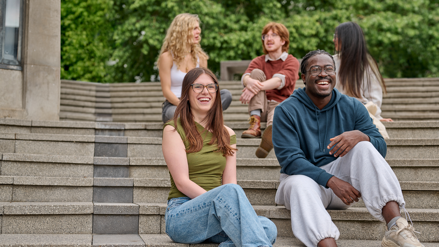 Five chatting and laughing students sit on steps.