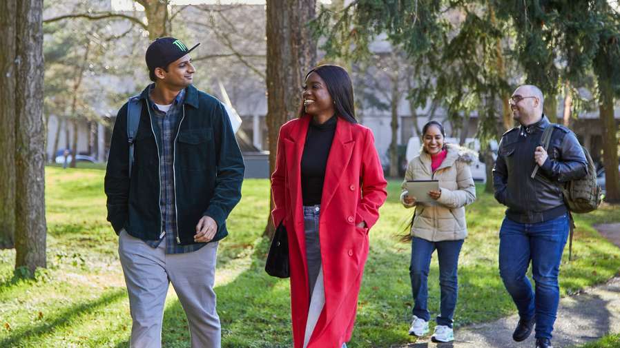 Four people walking and chatting happily, dressed in casual clothes, with trees and grass in the background."