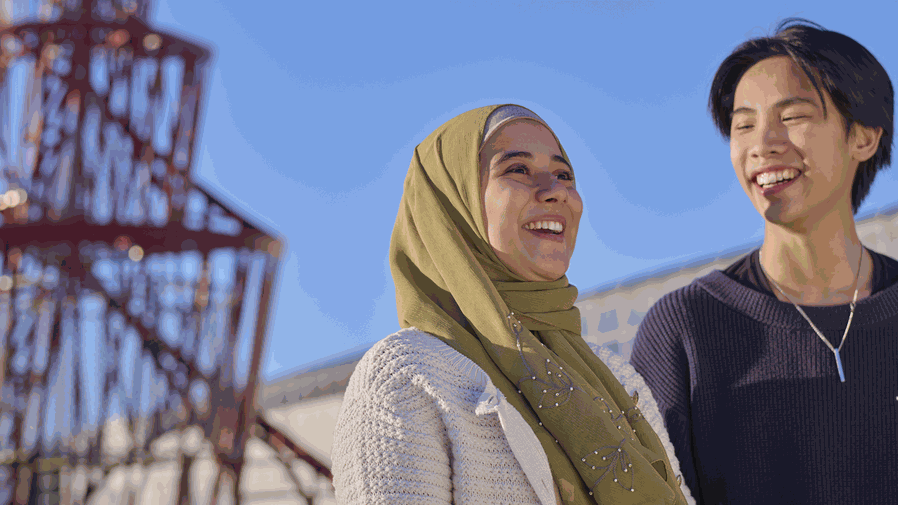 Two smiling students outside with a red sculpture behind them.