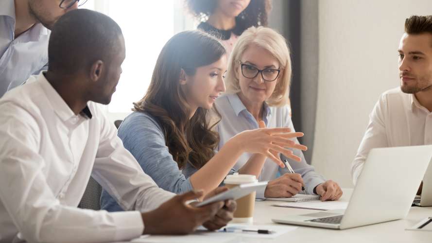 Young female mentor leader coach teaching employees group analyzing online project explaining business strategy speaking training diverse corporate team with laptop using computer at office meeting