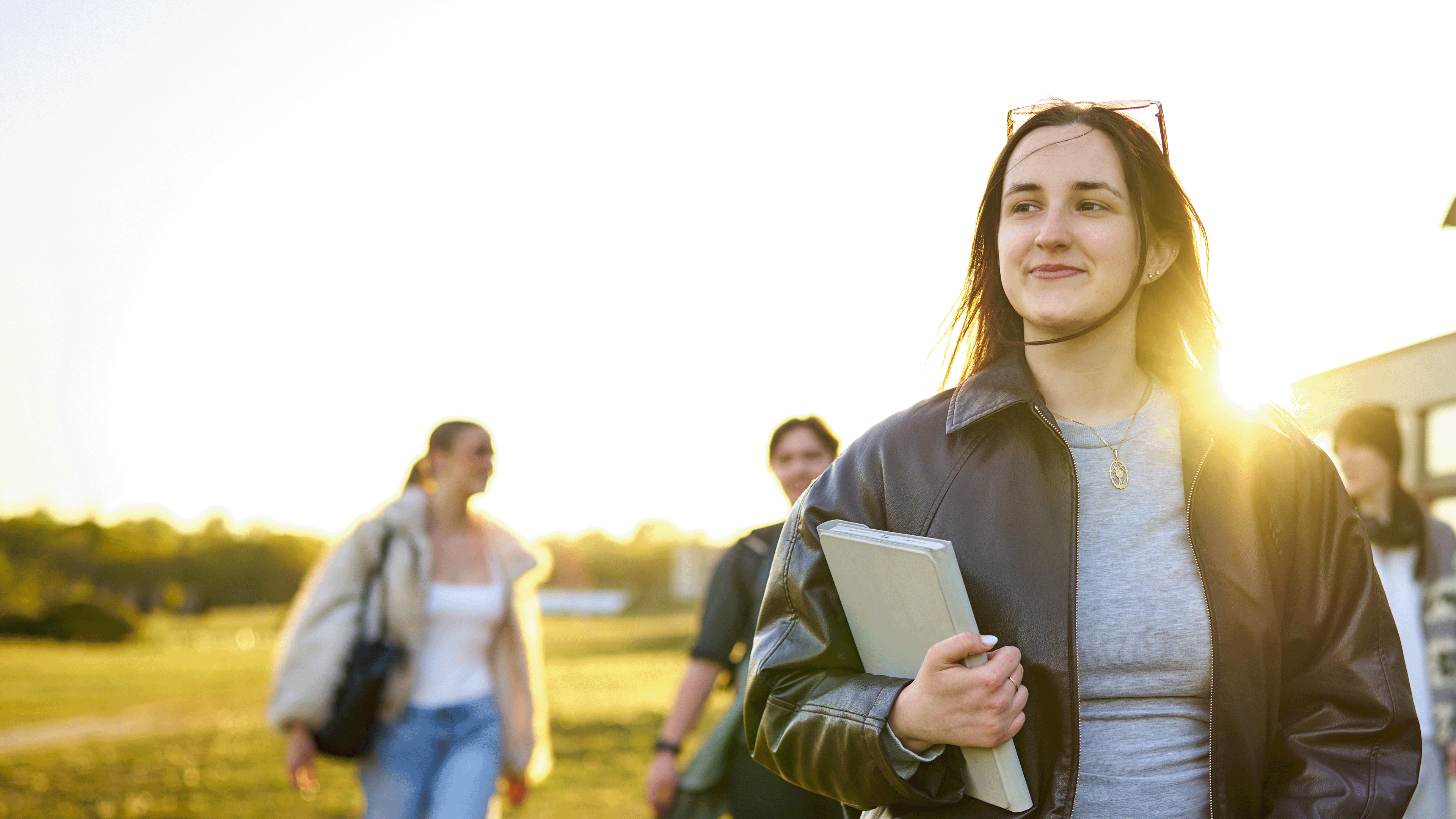 A student walks across a field on campus. Behind them there are other students.