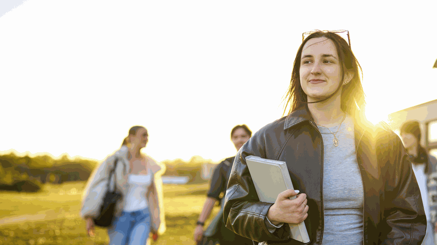 A student walks across a field on campus. Behind them there are other students.