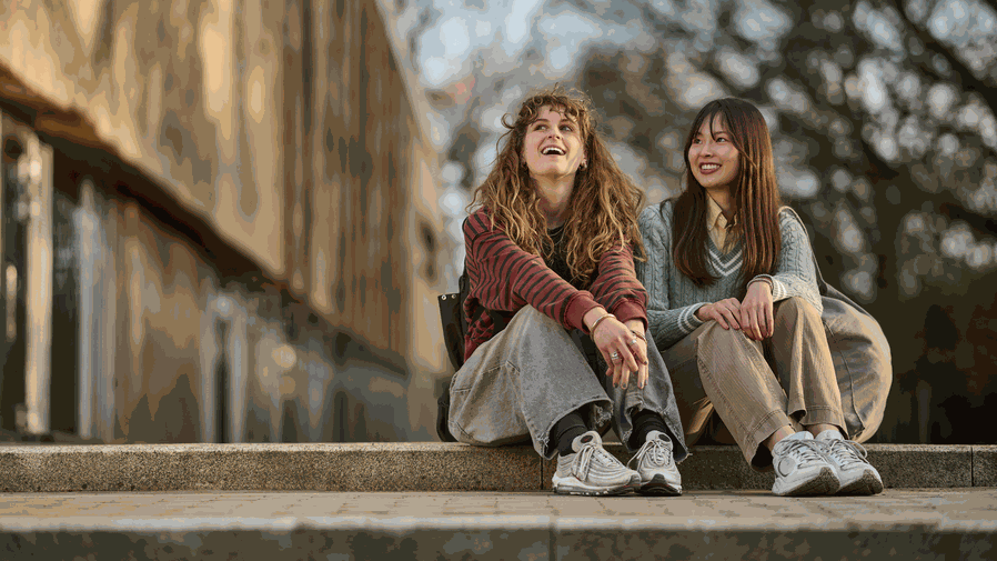 Two smiling students sit on some steps.