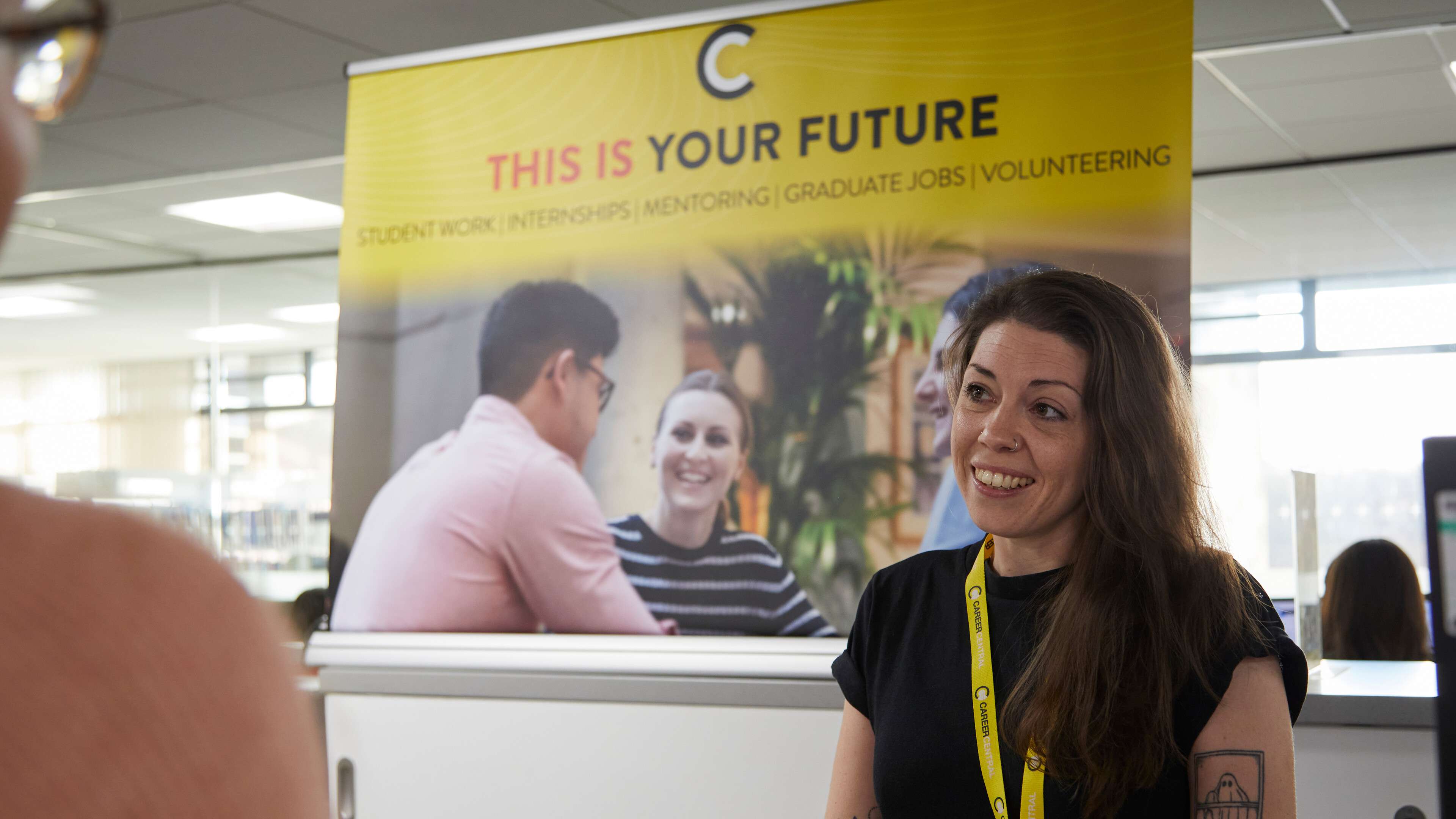 A member of the CareerCentral staff chats to somebody in front of a CareerCentral banner.