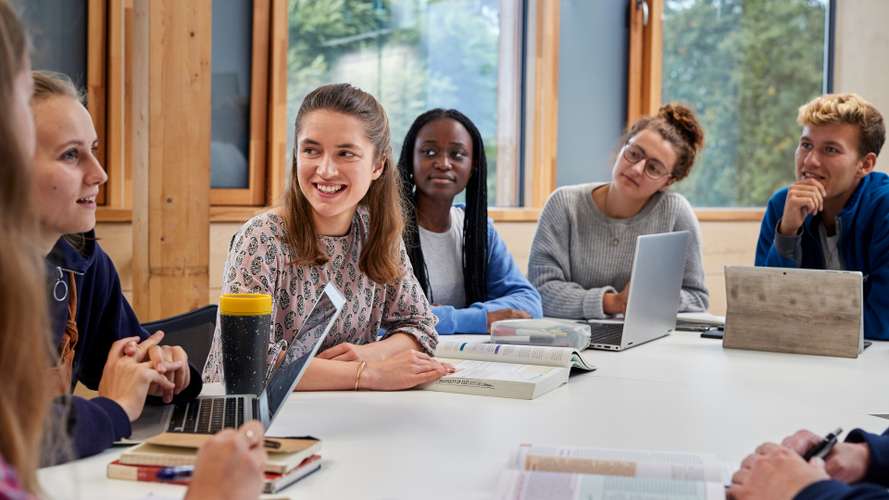 Students sat around a table with books and laptops