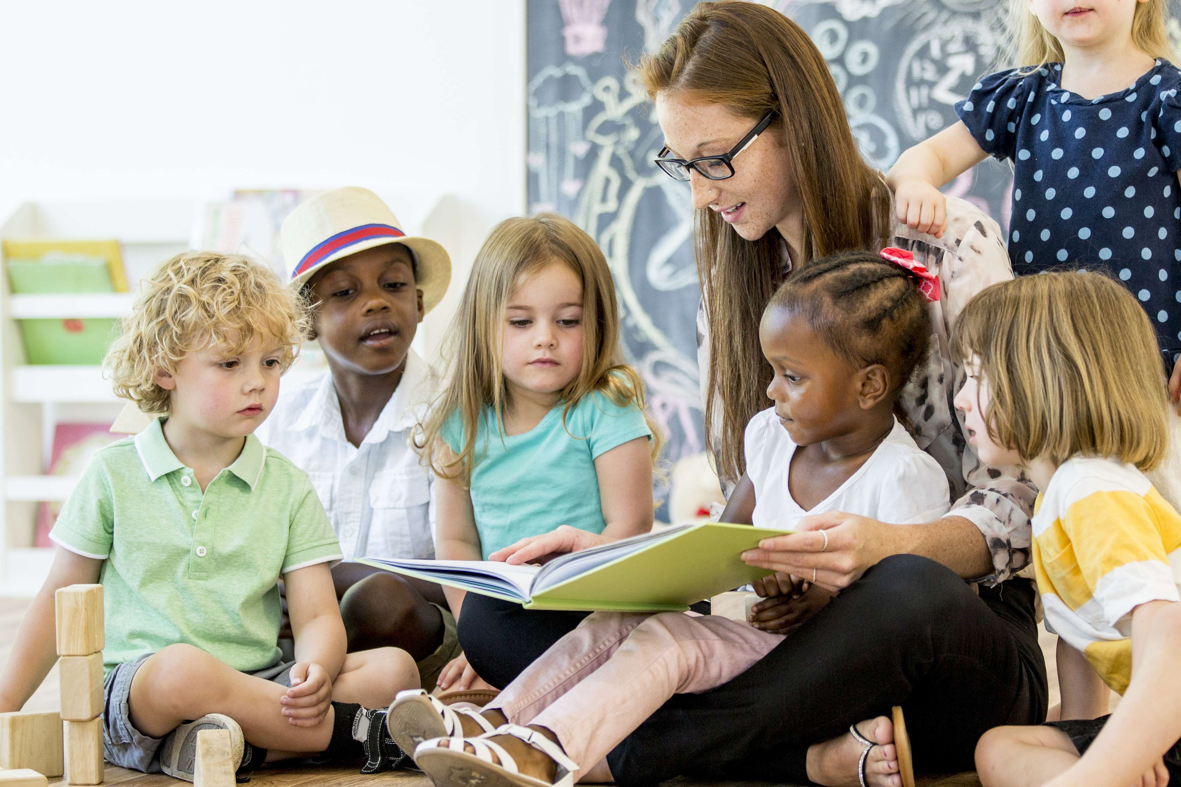 Group of young children with female teacher reading to them