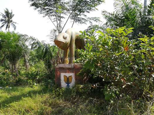 A green and yellow sculpture of a lizard amongst heavy foliage.