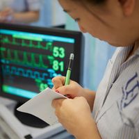 Student nurse taking notes next to monitor screen