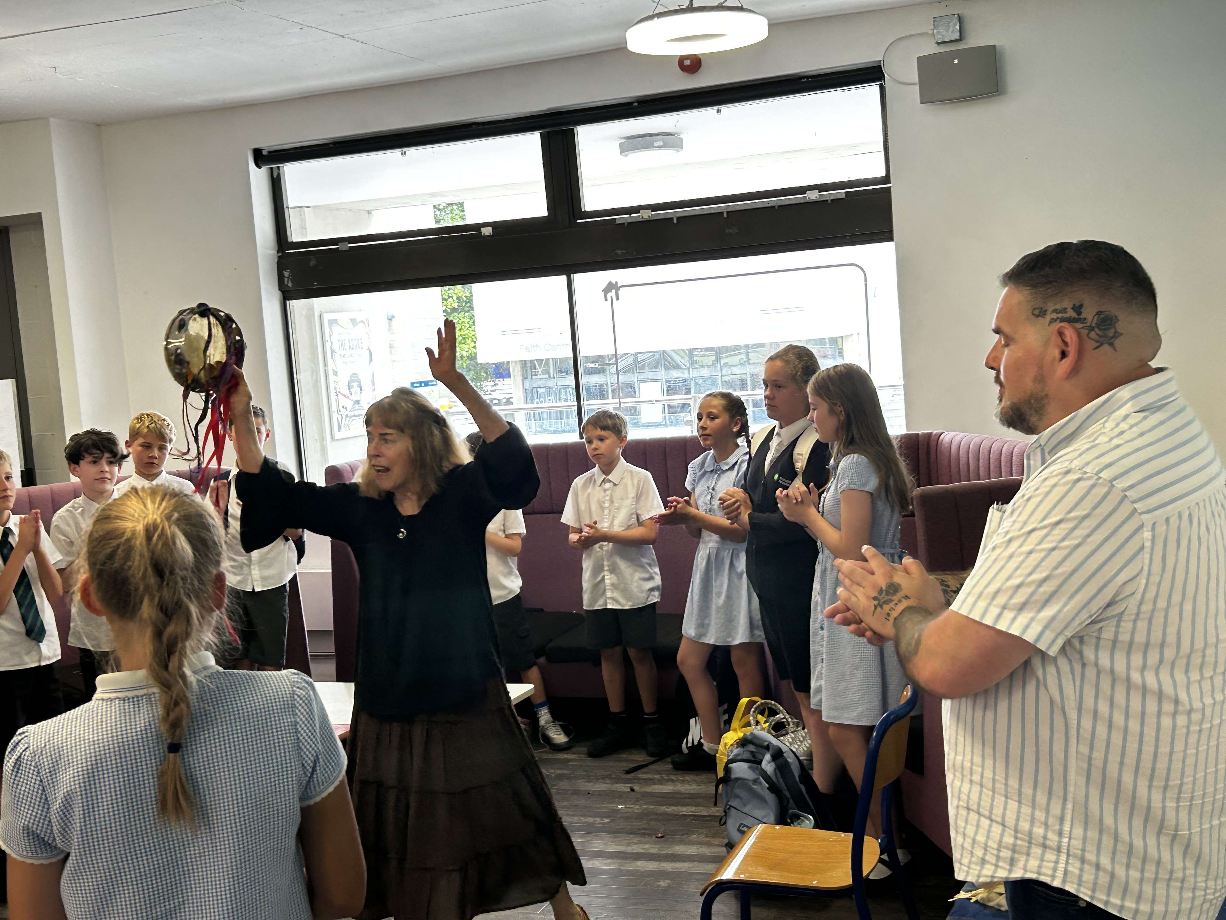 A researcher facilitates an interactive music workshop for schoolchildren, engaging them with a tambourine.