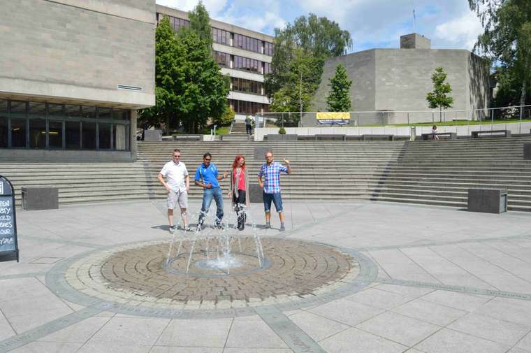 Four people in the UEA Square with a water fountain in front