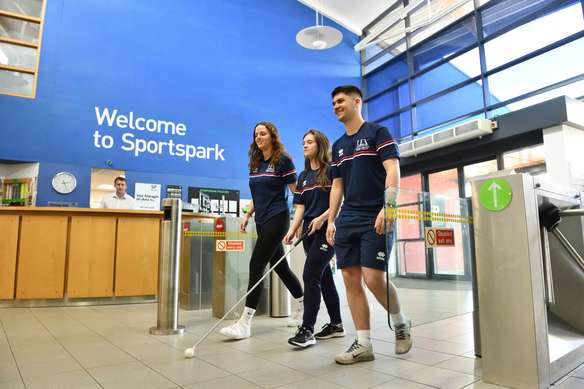 Three students walking in the Sportspark foyer, one using a white cane