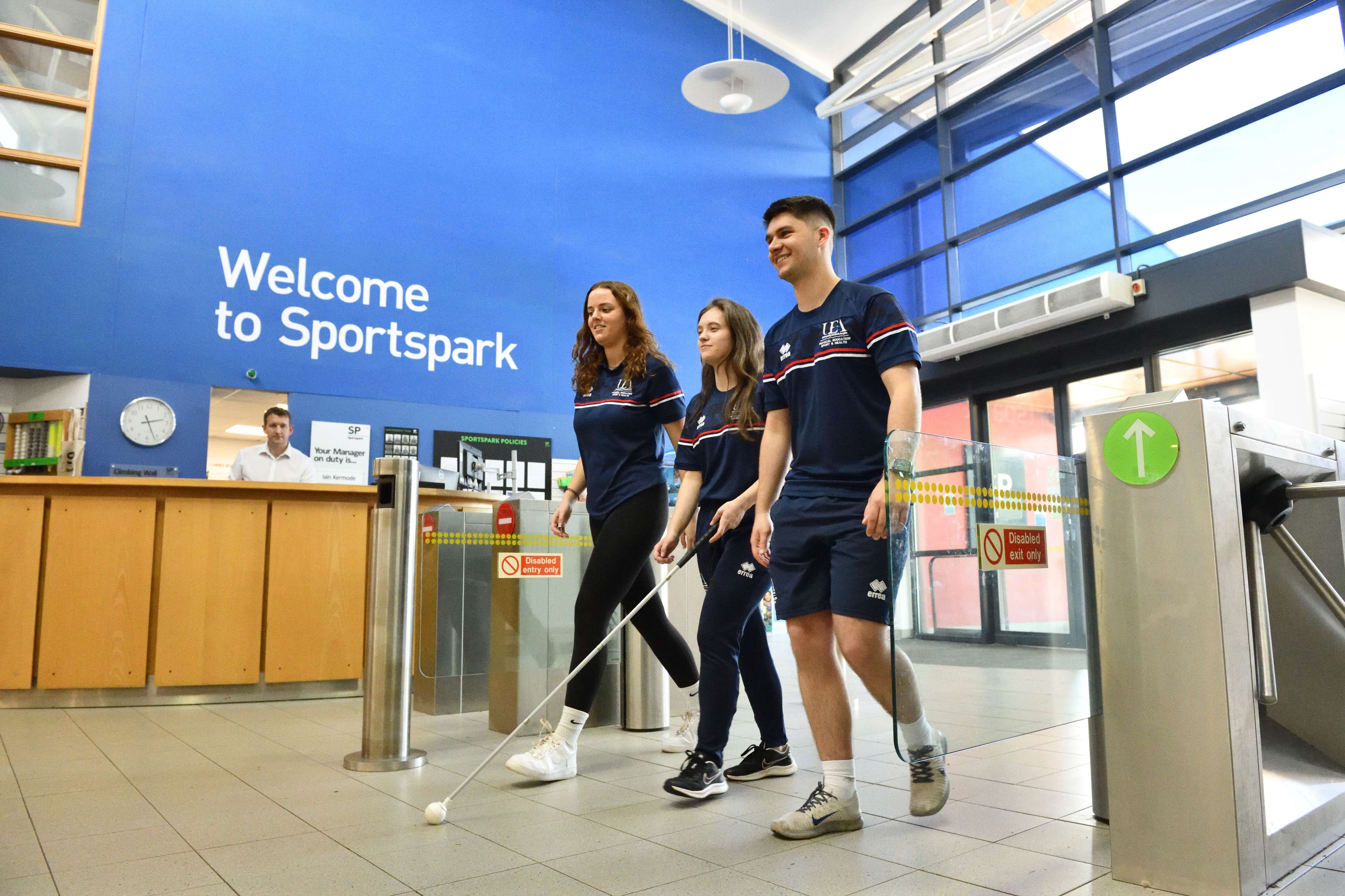 Three students walking in the Sportspark foyer, one using a white cane