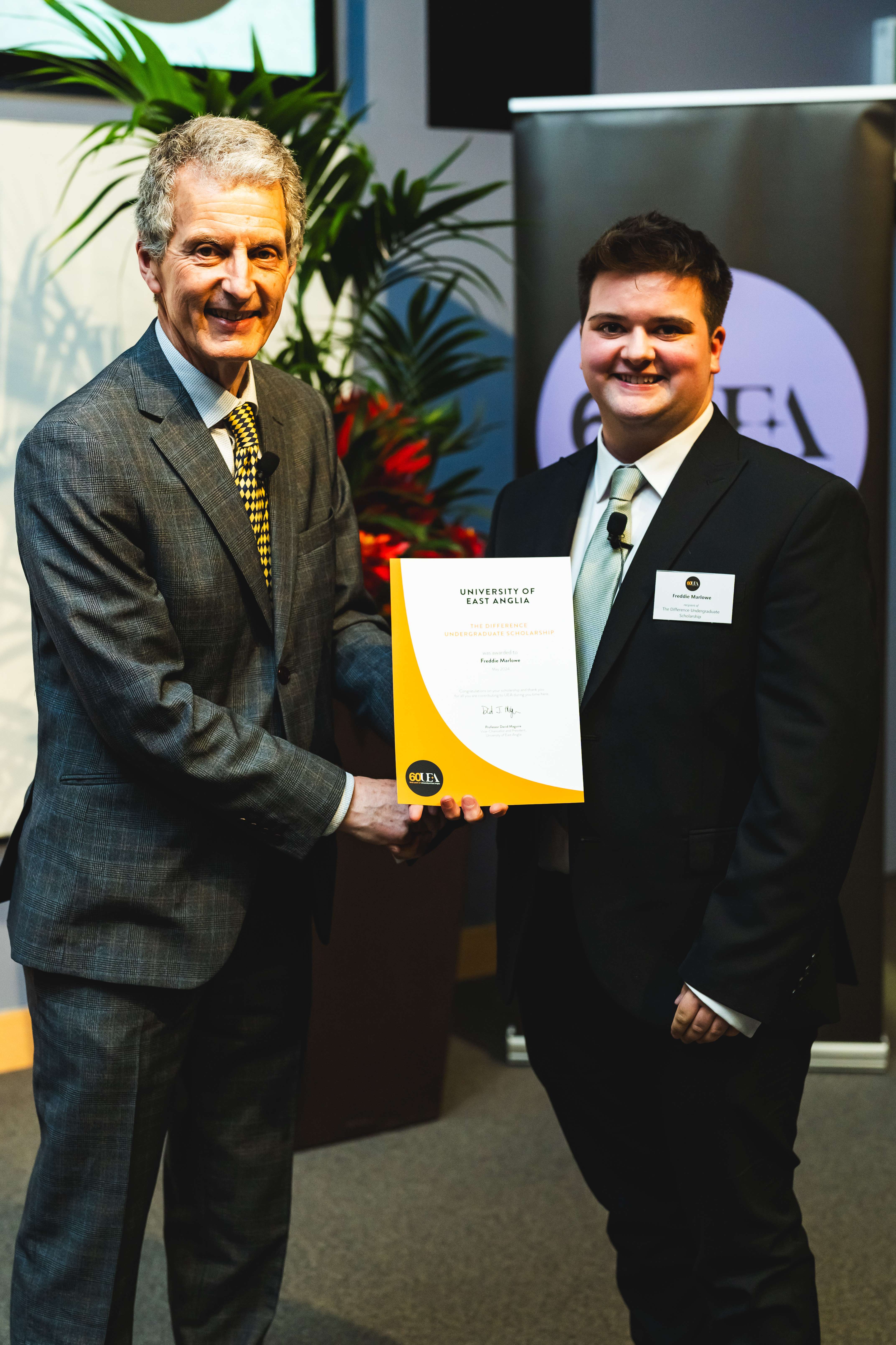 Freddie and UEA Vice-Chancellor and President Professor David Maguire shake hands at UEA's 60th Anniversary Scholarship Reception, both smiling as they celebrate the event.