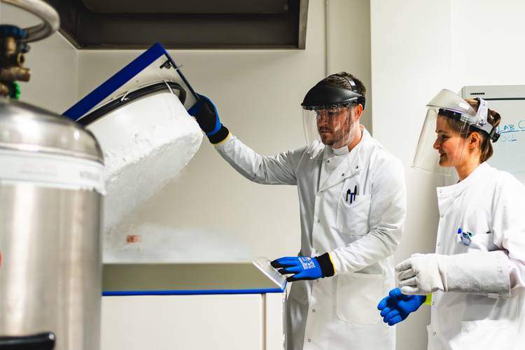 Emma Bull and Dr Darrell Green working in a laboratory, both wearing white lab coats, blue gloves, and protective face shields.