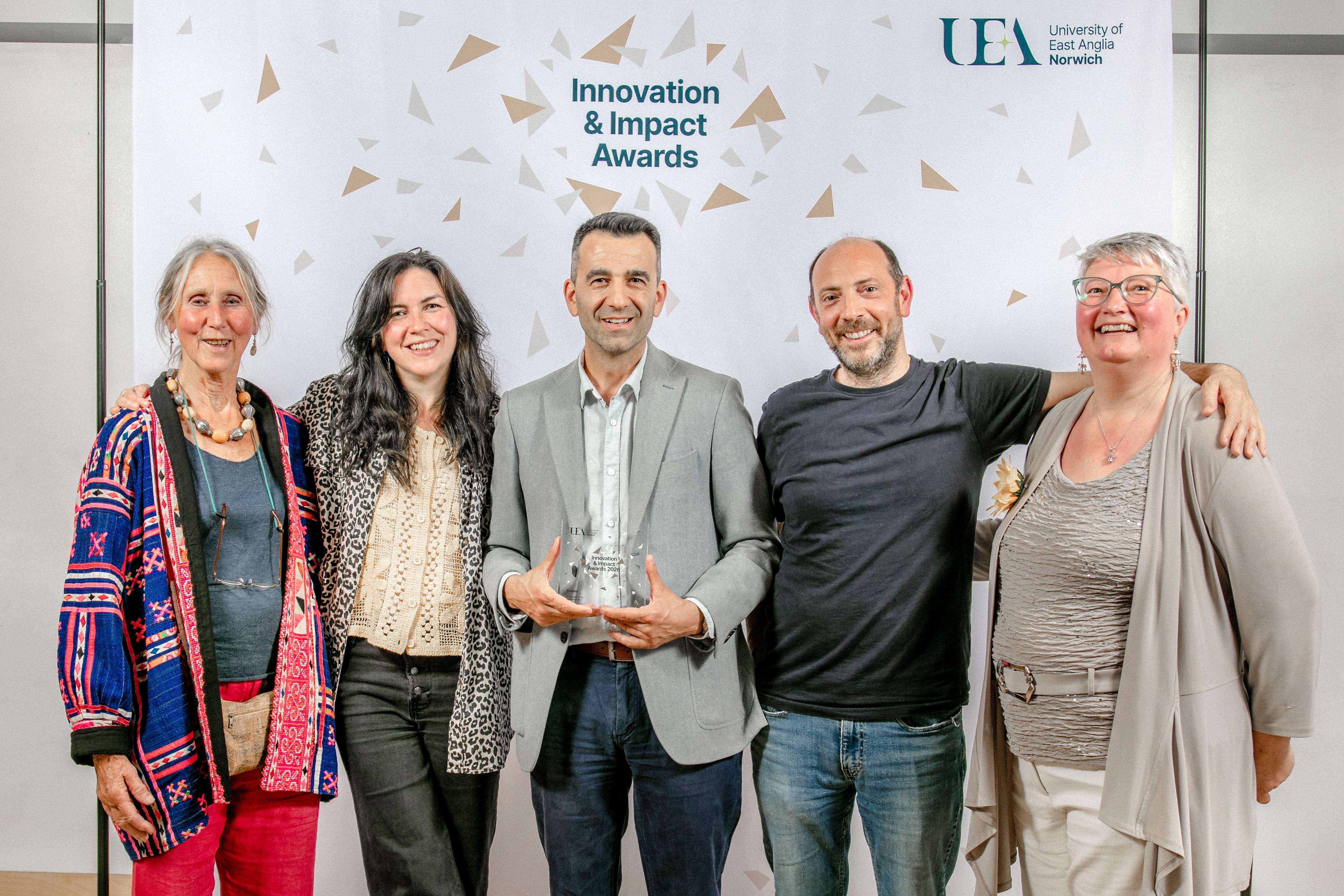A diverse team of five UEA researchers proudly holding their glass trophy at the university's Innovation & Impact Awards ceremony.
