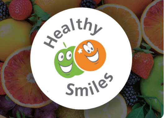Healthy Smiles logo with apple and orange smiling in the middle and a faded background of fruit