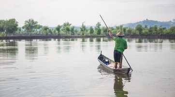 A person paddles a small boat on a calm lake