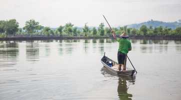 A person paddles a small boat on a calm lake