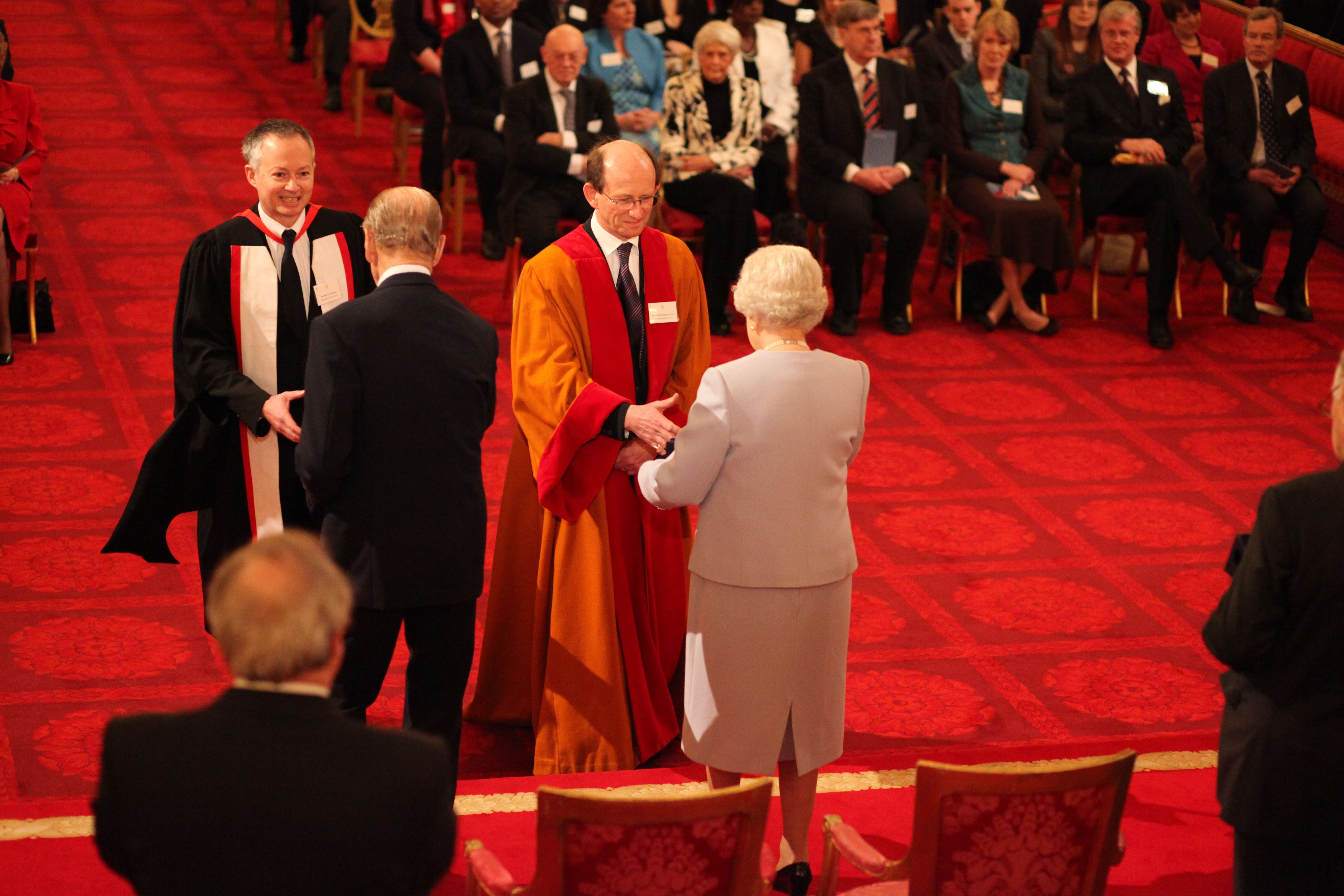 Queen Elizabeth presenting the award to a UEA staff member while Prince Philip shakes hands with another UEA staff member
