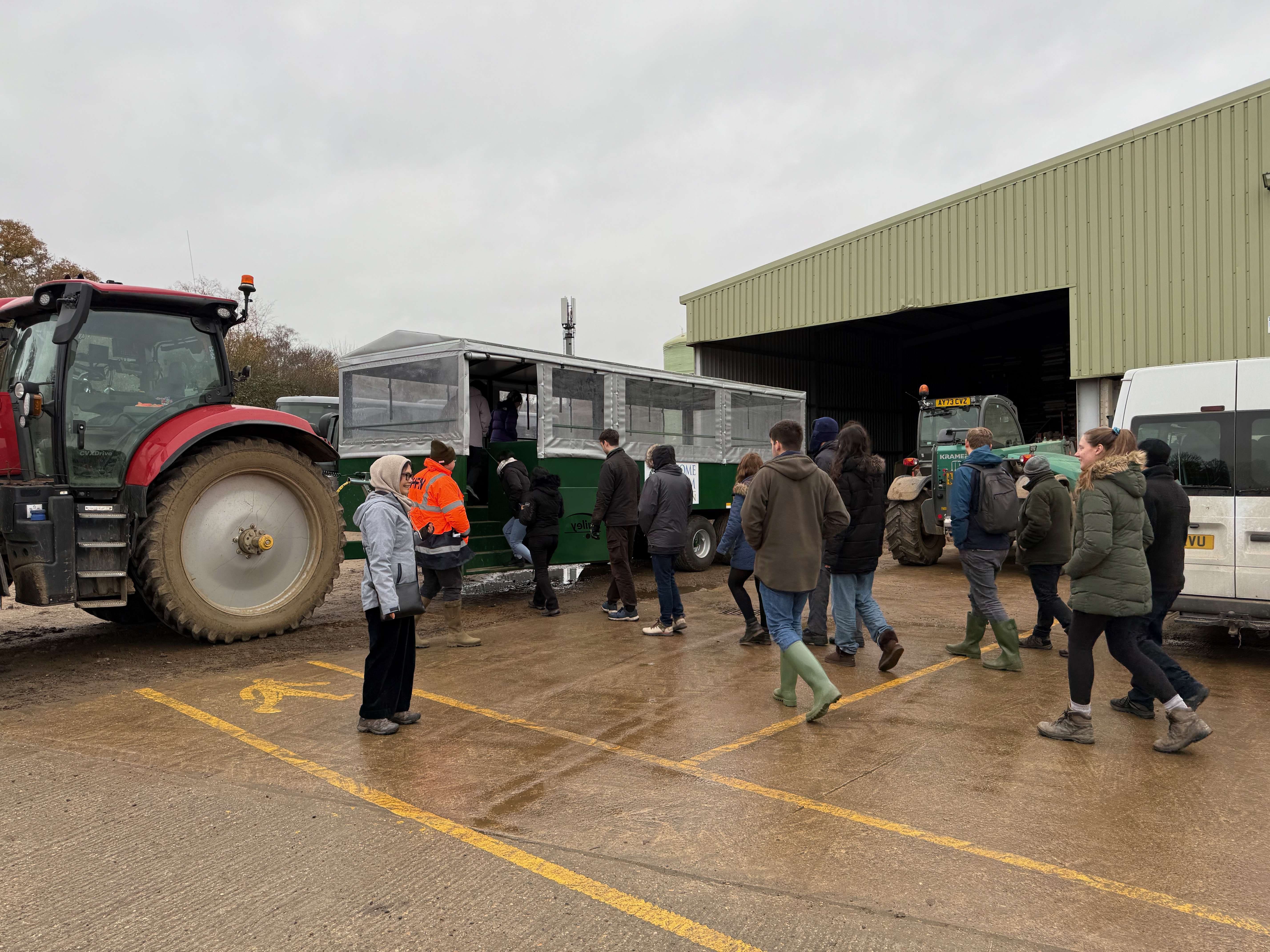 People in a queue getting on the trailer attached to the back of a tractor