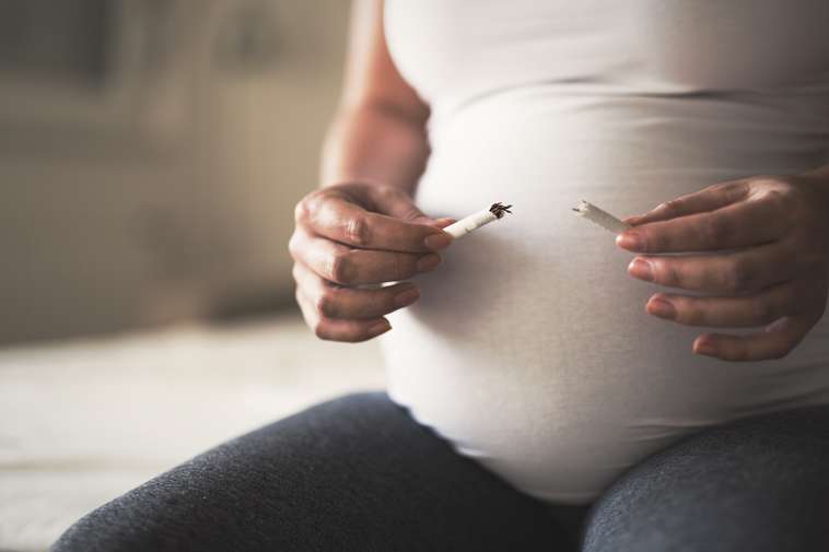 A pregnant person snapping a cigarette in half.