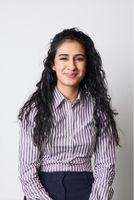 Person with long, curly hair wearing a striped shirt, smiling against a plain white background.