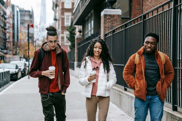 Content diverse friends with takeaway coffee walking on city street