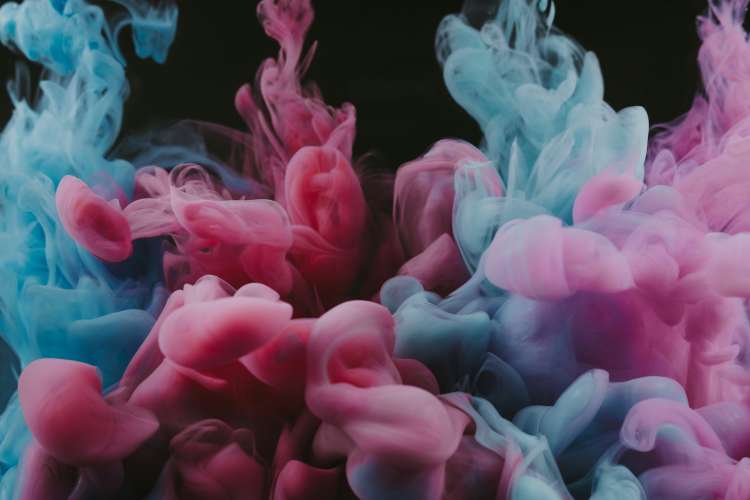 Swirling clouds of pink and blue smoke blend against a dark background, creating a vibrant and dynamic abstract pattern.