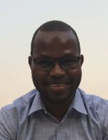Smiling man wearing glasses and a light blue shirt against a clear sky backdrop.
