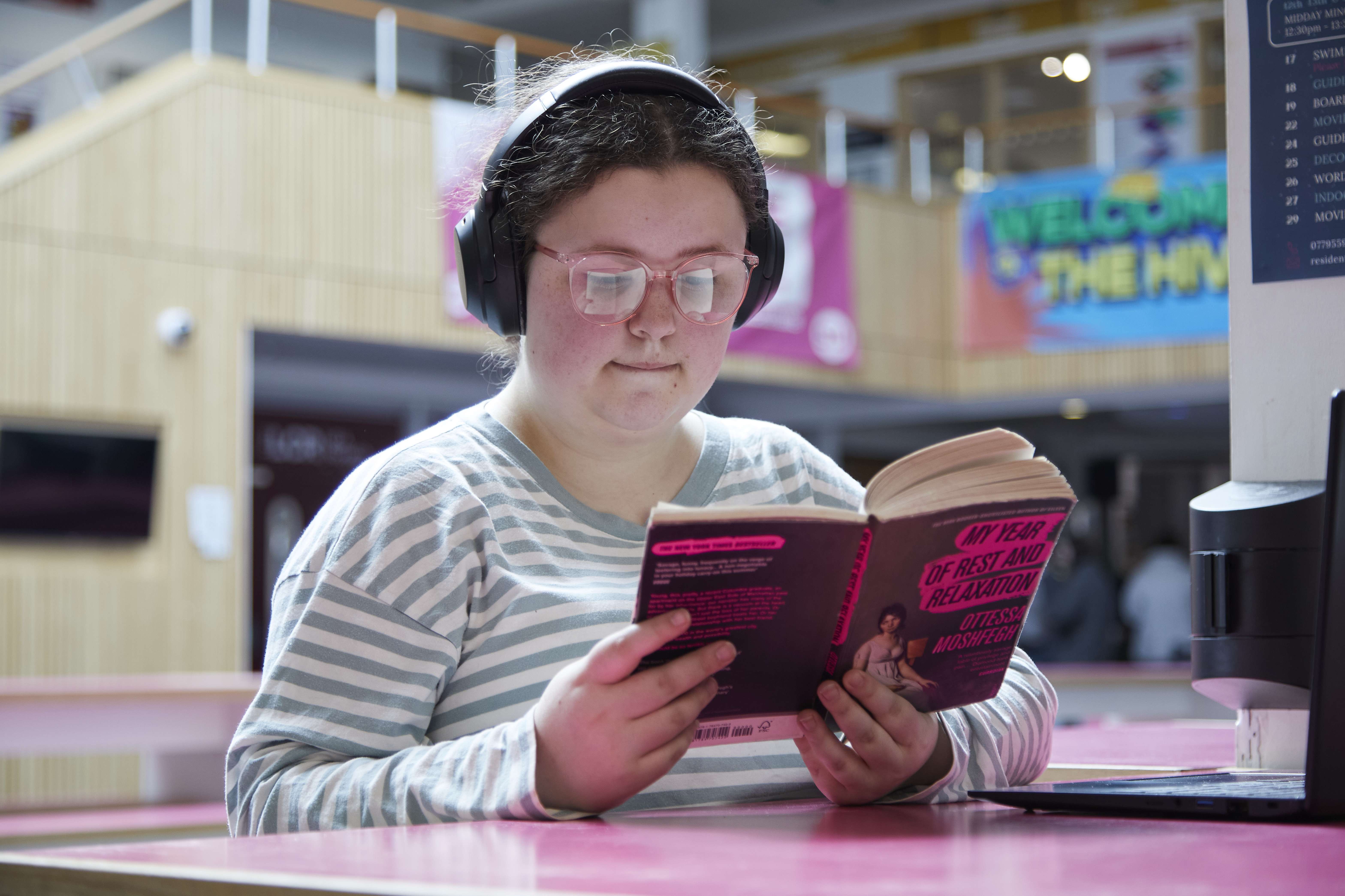 student reading a book, wearing headphones