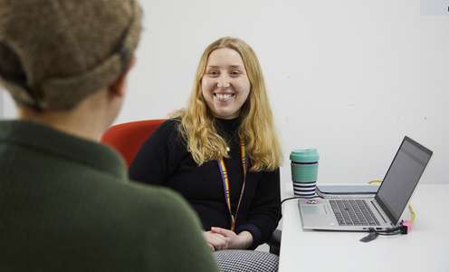 Staff member with laptop chatting to student opposite them