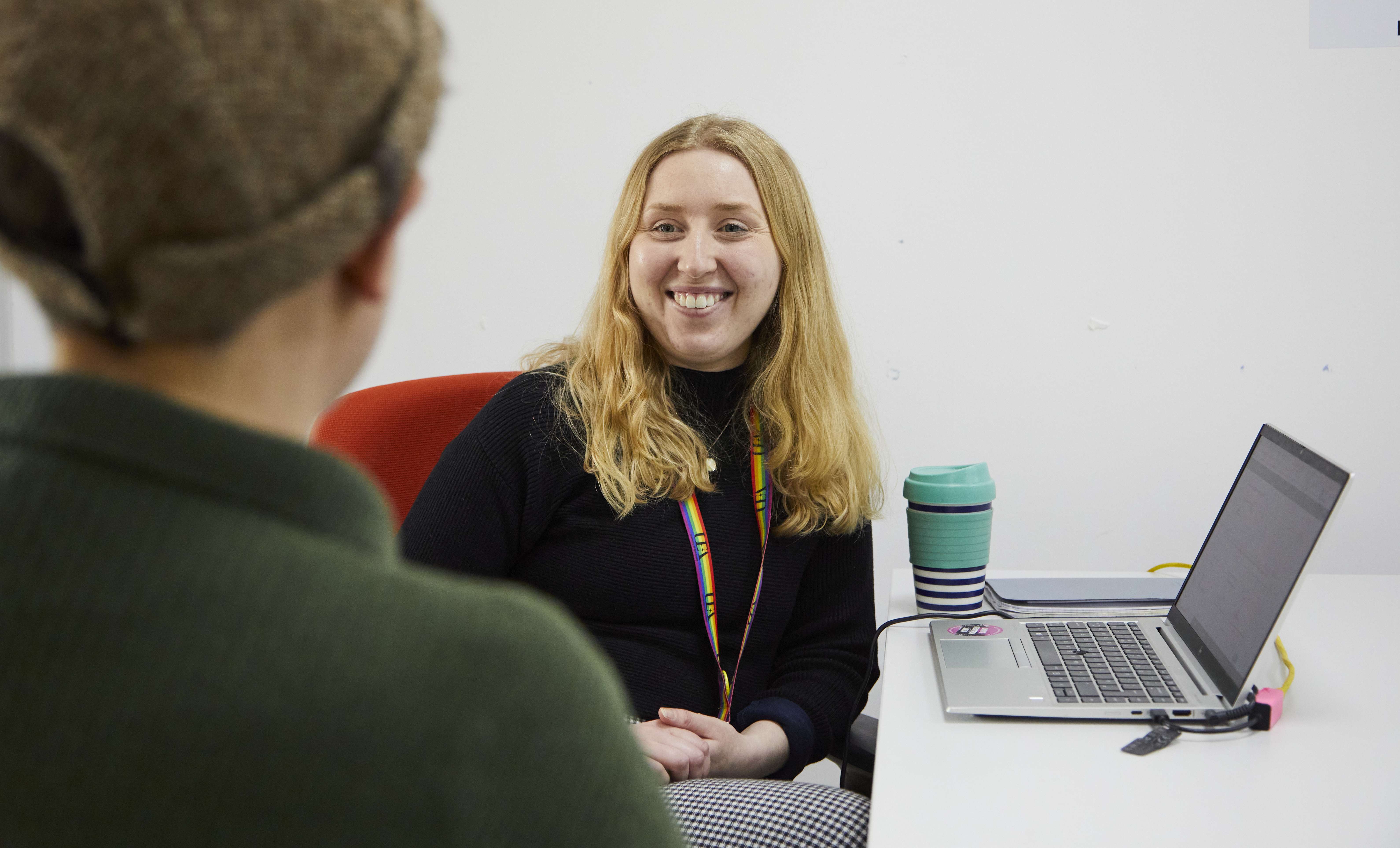 Staff member with laptop chatting to student opposite them