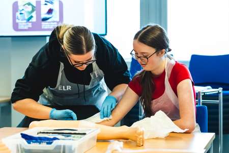Children and Young People Nursing students taking part in a learning session focused on wound care. The session includes a brief demonstration of ANTT (Aseptic Non Touch Technique) and wound care, followed by students practising the technique on both manikins and each other.
