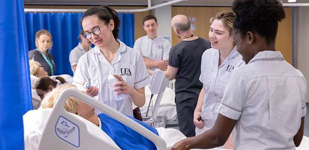 Nursing students in uniforms practicing patient care on a hospital bed healthcare model in a clinical skills lab, smiling and collaborating.