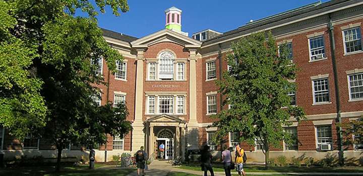 A red brick building with green trees and people walking in the foreground.