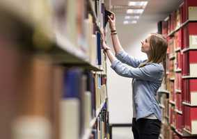 Person in a library reaching up for a book on a shelf
