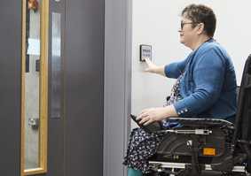 A wheelchair user uses a push pad to open a powered door