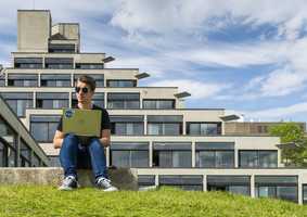 Student on laptop sitting outside Ziggurat on a Spring Day