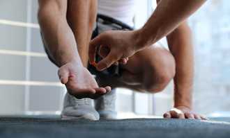 A person kneels, extending a hand to receive a pill from another person's hand in a bright indoor setting.