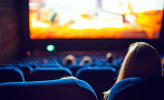 Audience watching a movie in a theater with blue seats and a brightly lit screen in the background.