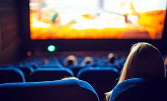 Audience watching a movie in a theater with blue seats and a brightly lit screen in the background.