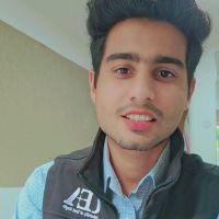 Close-up of a smiling young man with dark hair and light stubble, wearing a collared shirt and zip vest.