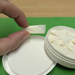A tub of nicotine pouches on a green background. The tub is resting at a jaunty angle.